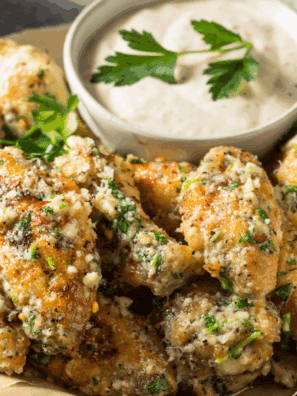 Golden air fryer garlic parmesan wings on a plate topped with melted butter, garlic, and grated Parmesan cheese.