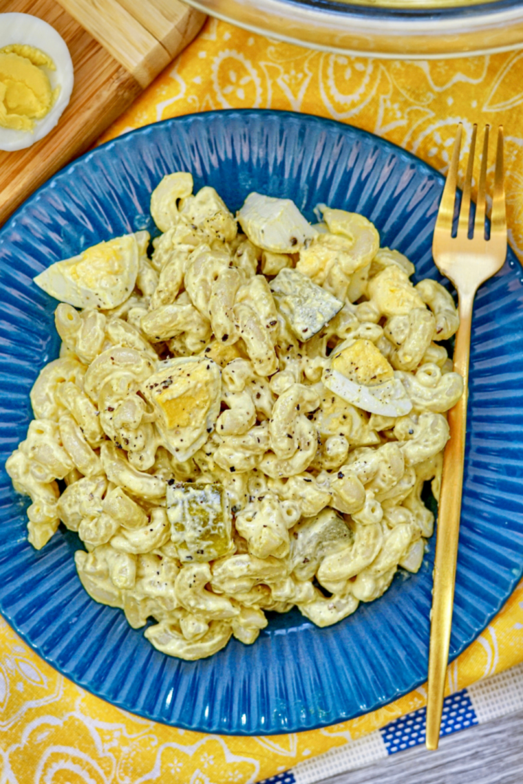 Creamy deviled egg pasta salad in bowl with paprika garnish, mustard dressing, chopped eggs, and pasta mixed together.