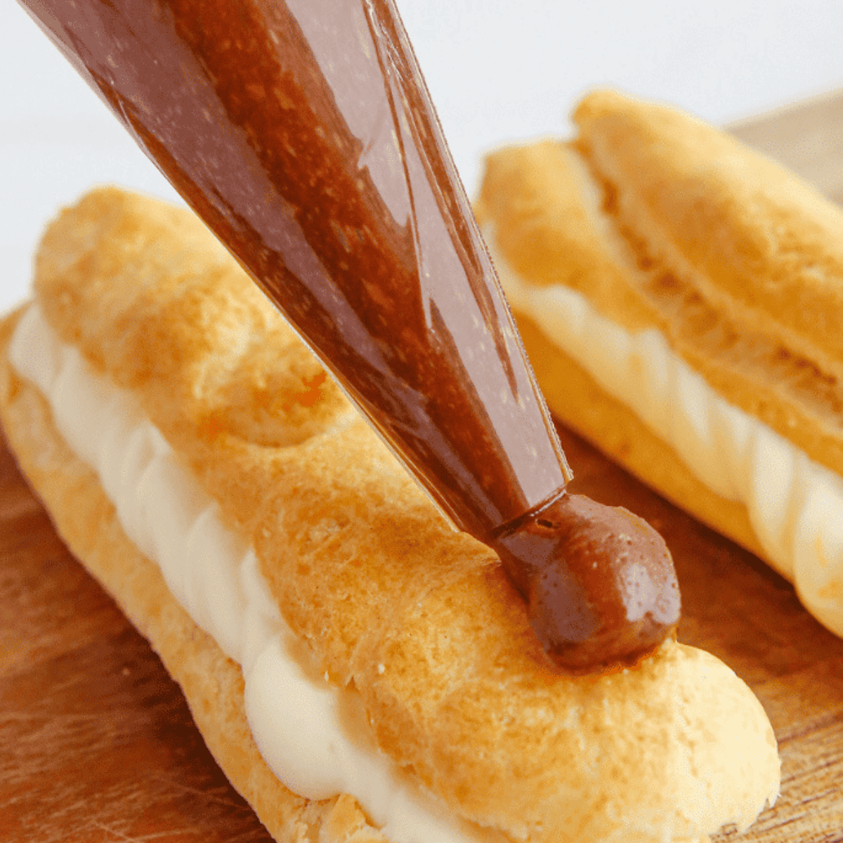 Air Fryer eclairs filled with creamy custard and topped with a shiny chocolate glaze, arranged on a plate.