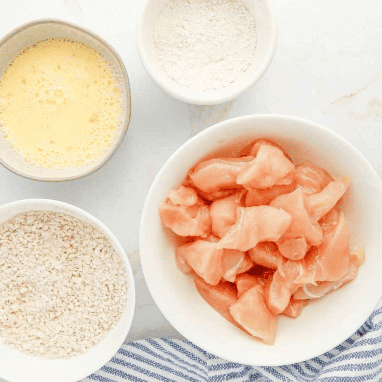 Three-bowl breading station with flour mixture, beaten eggs, and seasoned panko breadcrumbs set up for coating popcorn chicken before air frying