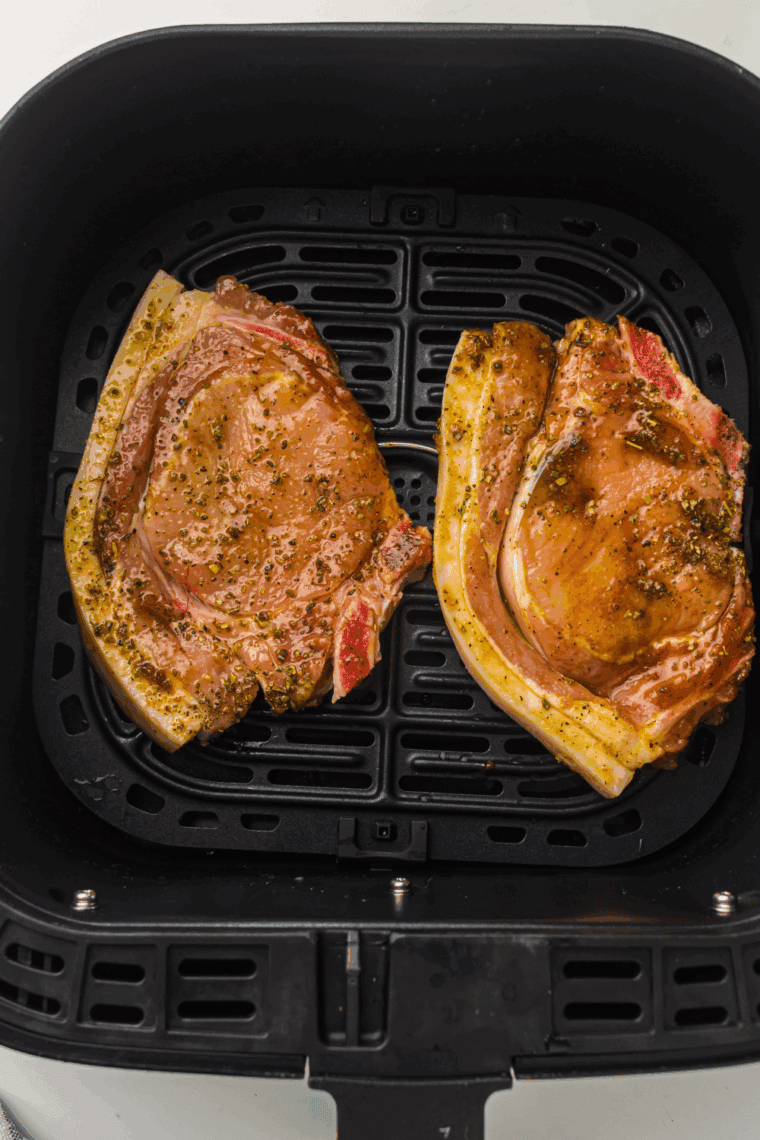 Seasoned ranch pork chops arranged in a single layer in the air fryer basket