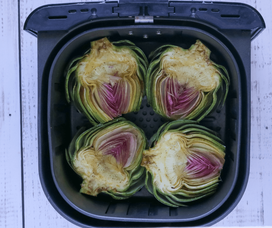 Seasoned artichoke halves arranged cut side down in an air fryer basket