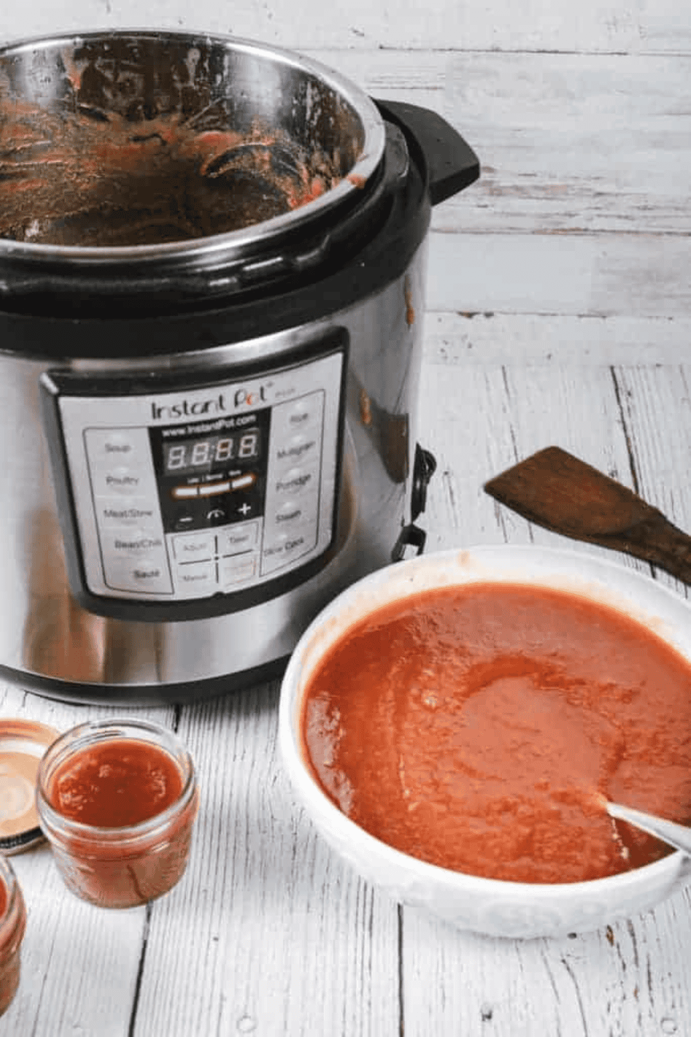 Jar of homemade Cracker Barrel apple butter surrounded by fresh apples and warm spices