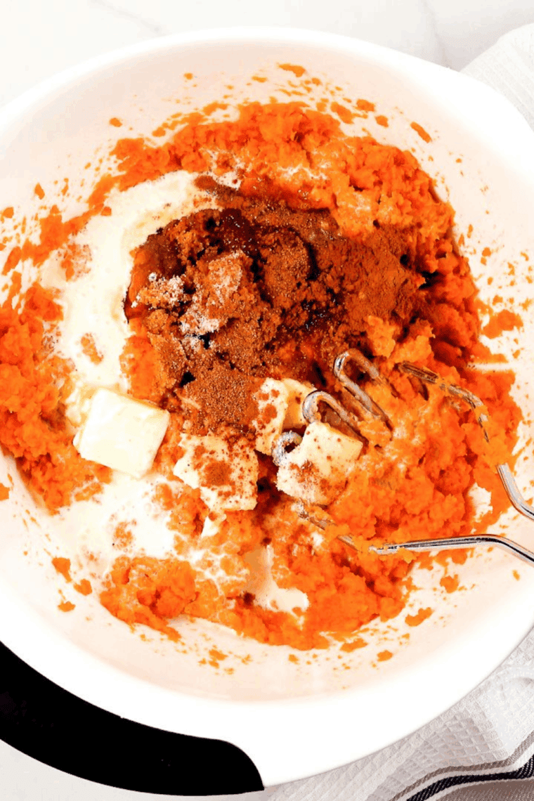 Mashing drained canned yams with brown sugar and spices in a glass mixing bowl