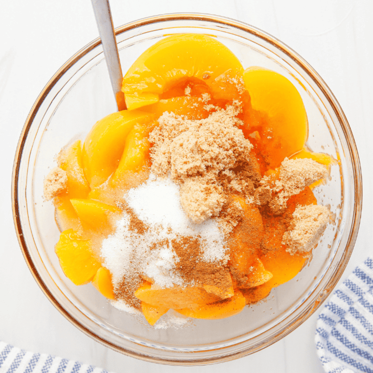Sliced peaches mixed with sugar, flour, cinnamon, and nutmeg in a bowl, coated evenly for peach cobbler filling.