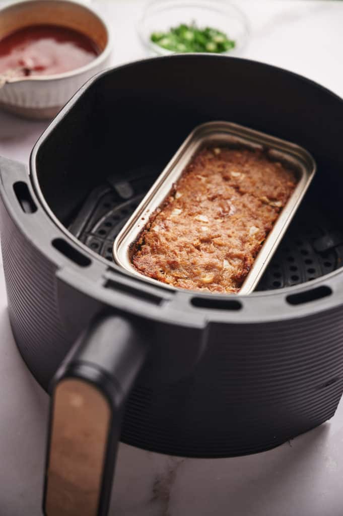 Preparing mini loaf pan with cooking spray or olive oil, then adding meatloaf mixture; alternatively, shaping meatloaf loaf on parchment paper in air fryer basket.