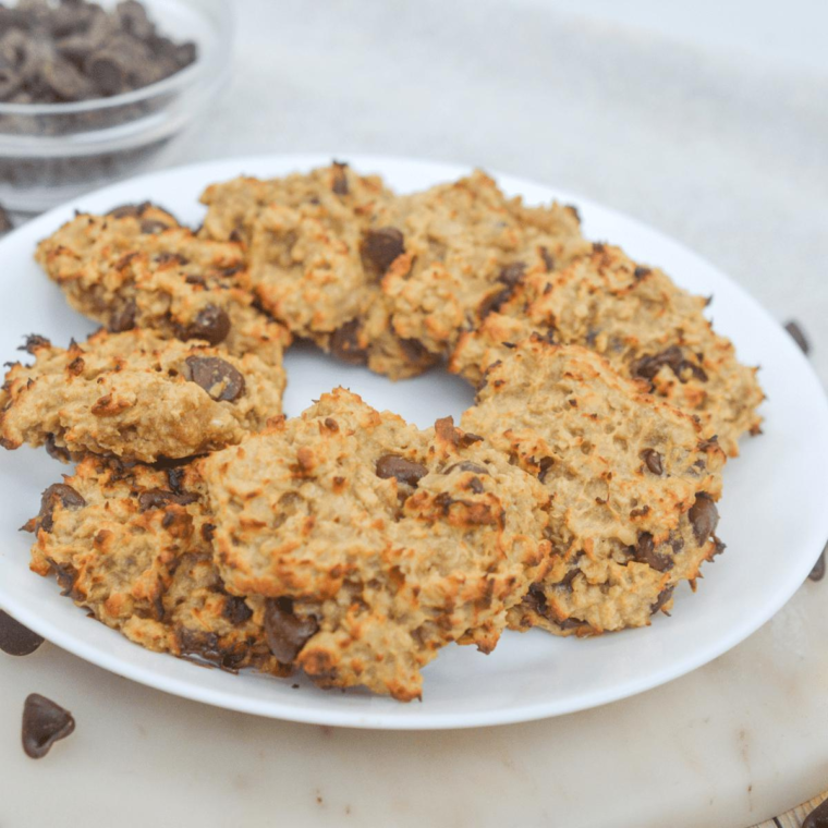 Air fryer banana bread cookies stacked on a wooden board with chocolate chips and a ripe banana