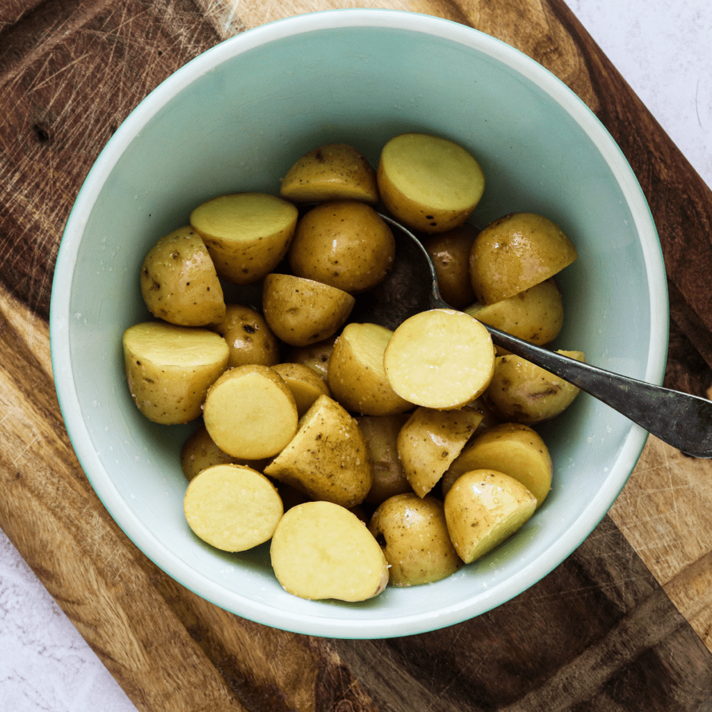 Washing and drying baby potatoes, cutting in half, and tossing with olive oil and salt to coat