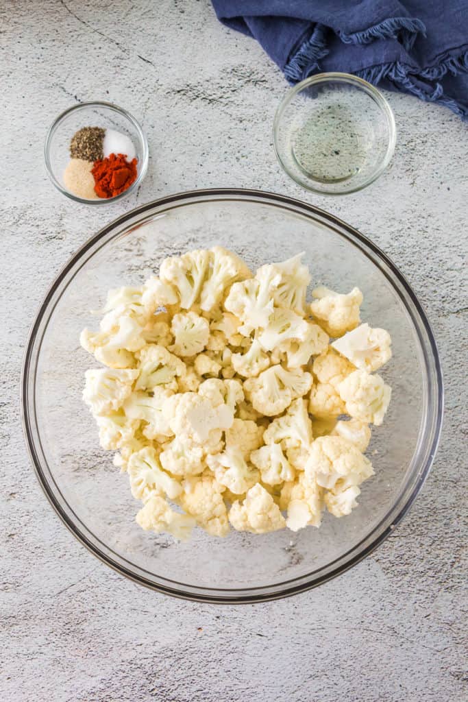The ingredients for the Air-Fryer Tandoori Cauliflower are arranged on a countertop, including cauliflower florets, yogurt, tandoori spices, garlic, ginger, and lemon juice.