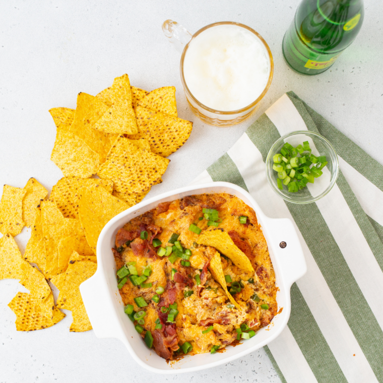 Air fryer jalapeño popper dip served with tortilla chips and a cold beer on a wooden table, set up for game day