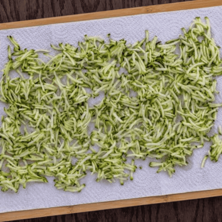Grated zucchini on a paper towel being salted and squeezed to remove excess moisture before making air fryer zucchini tots.