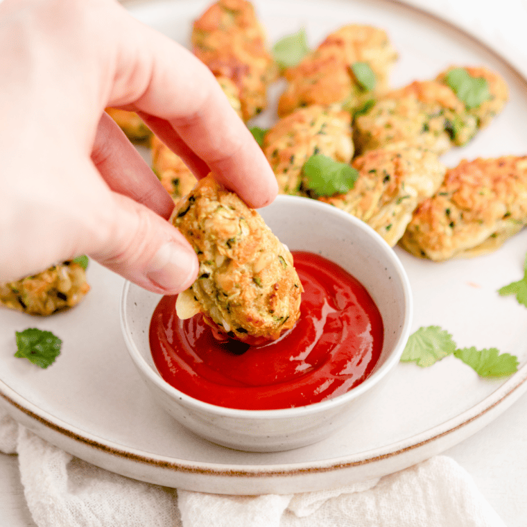 Golden brown air fryer zucchini tots served on a white plate with dipping sauce and fresh herbs.