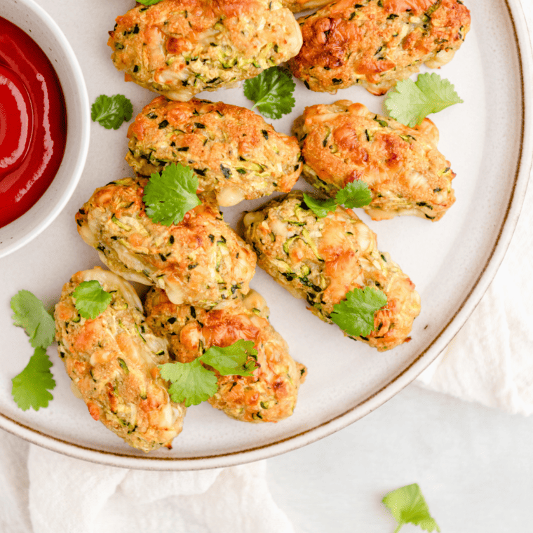 Golden brown air fryer zucchini tots on a plate, crispy on the outside and soft inside, served with a side of dipping sauce.