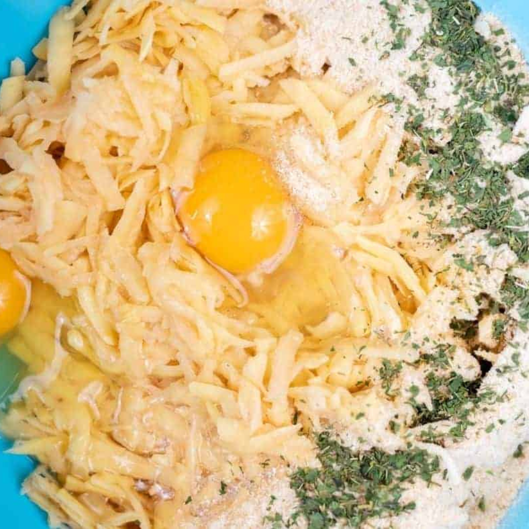 Bowl filled with grated zucchini, cheese, egg, bread crumbs, and seasonings being mixed together for zucchini tots.