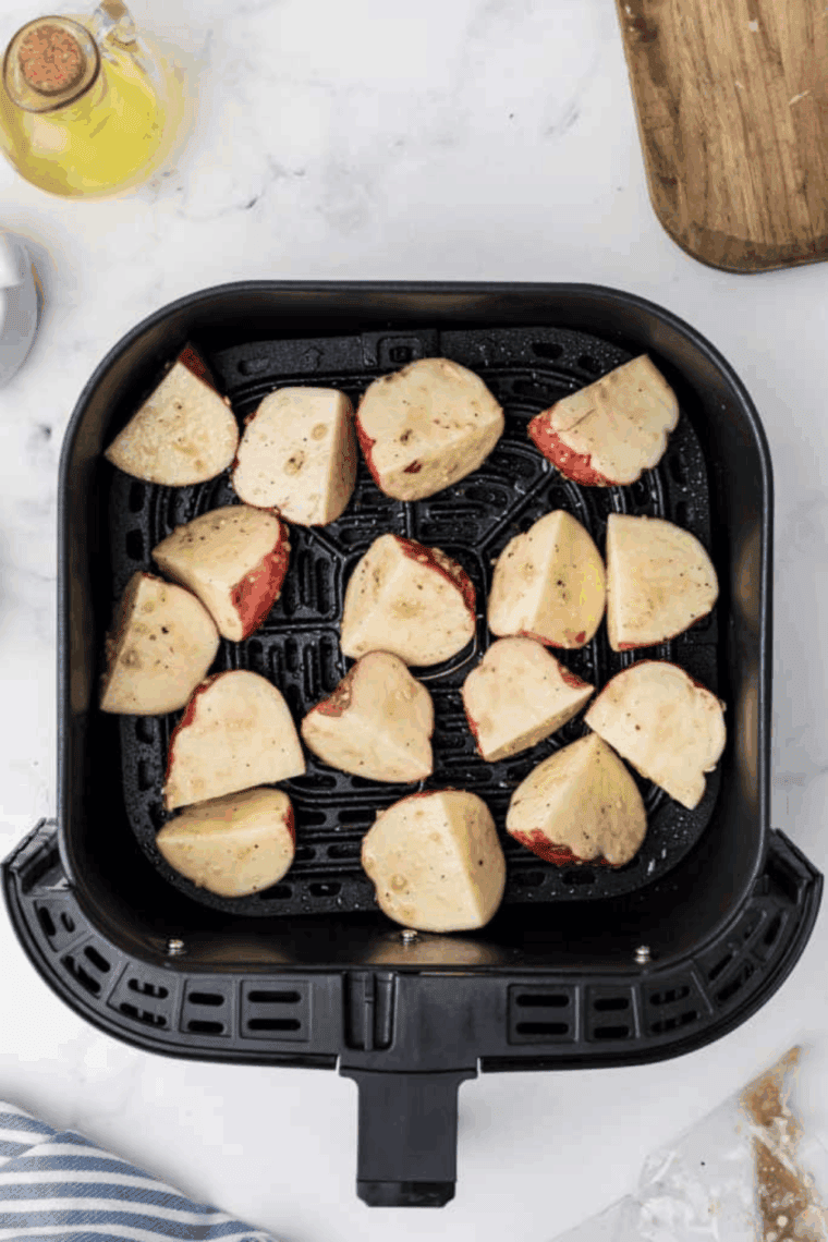 Pesto-coated potato cubes arranged in a single layer in the air fryer basket, cooking at 400°F until tender.