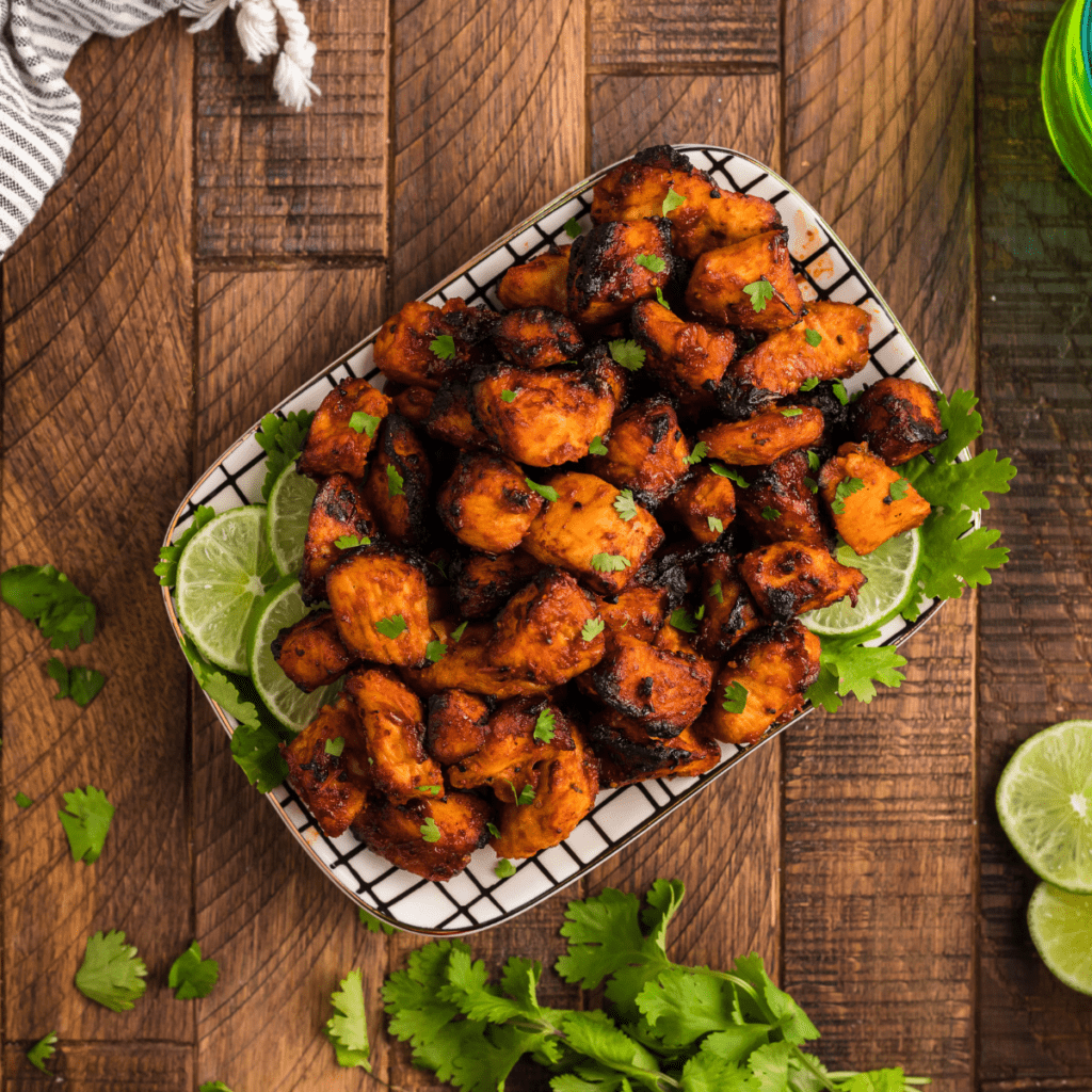 Crispy air fryer BBQ chicken bites coated in sticky barbecue glaze on a white plate.