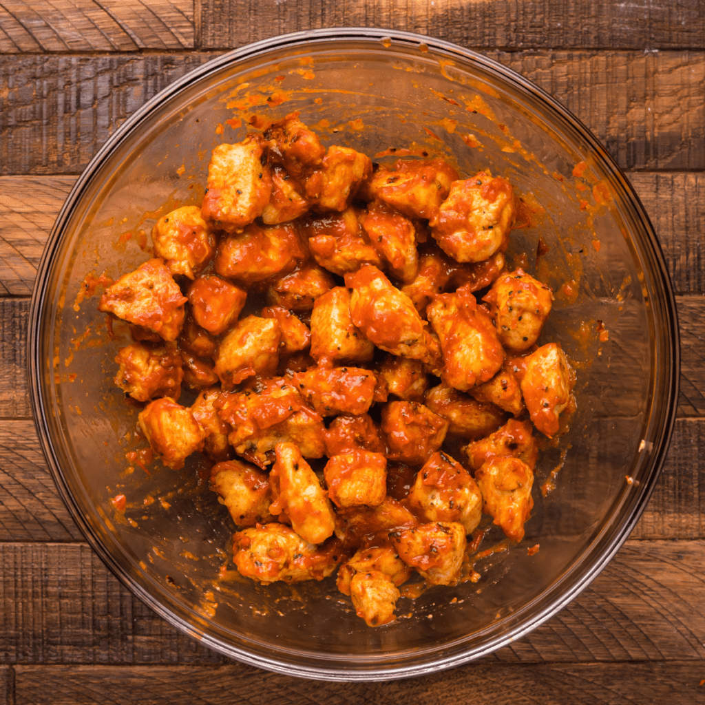 Air-fried chicken bites tossed in BBQ sauce in a glass bowl.