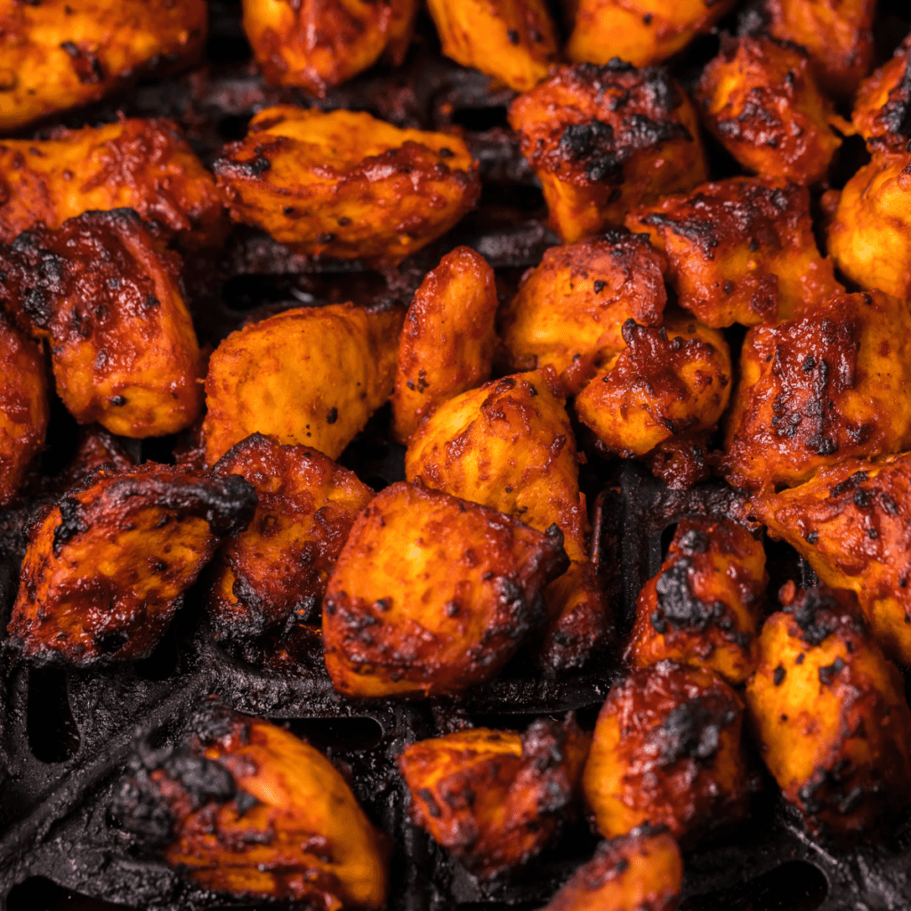 BBQ chicken bites in the air fryer basket as the sauce caramelizes.