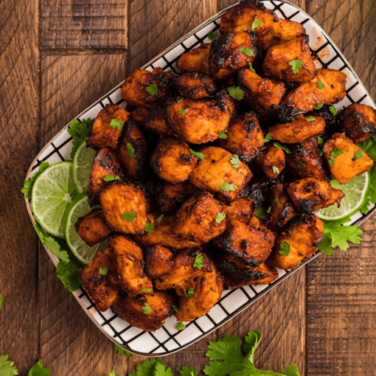Golden air fryer BBQ chicken bites garnished with fresh herbs on a plate.