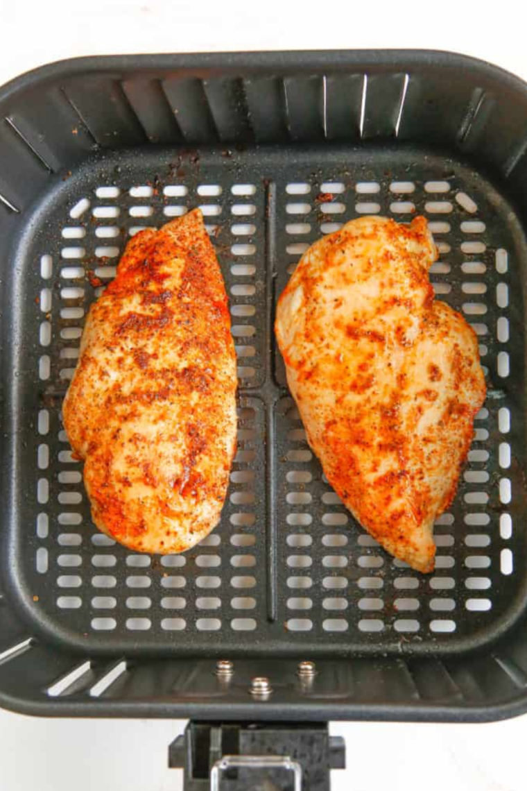 Seasoned chicken breasts placed in the air fryer basket, cooking at 375°F for an even golden brown finish.