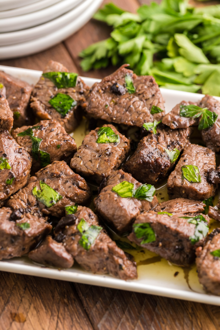 Golden brown steak bites coated in garlic butter cooking in an air fryer basket, sizzling and perfectly seared.
