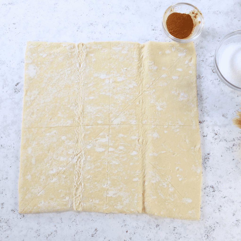 Cutting dough into squares and triangles on floured surface with pizza cutter for churro preparation.