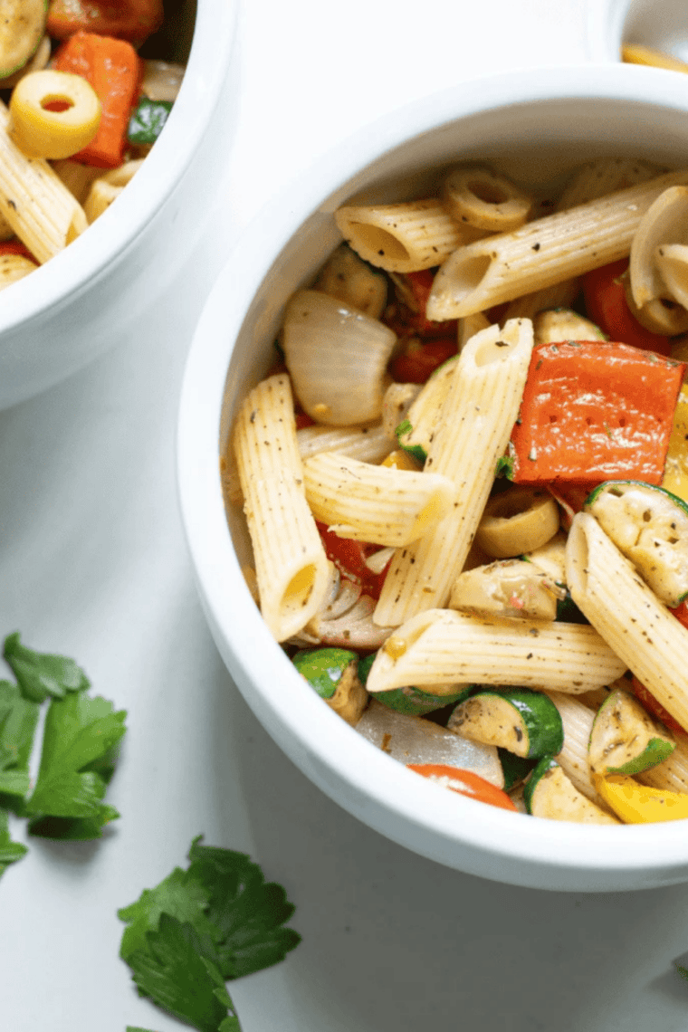 Air fryer pasta salad with roasted vegetables in a large white serving bowl, topped with cherry tomatoes, zucchini, bell peppers and kalamata olives