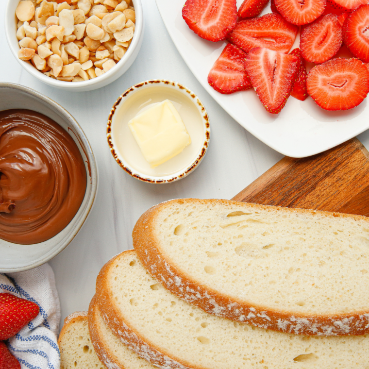 Ingredients for air fryer strawberry macadamia panini: butter, bread, strawberries, macadamia nuts, and Nutella