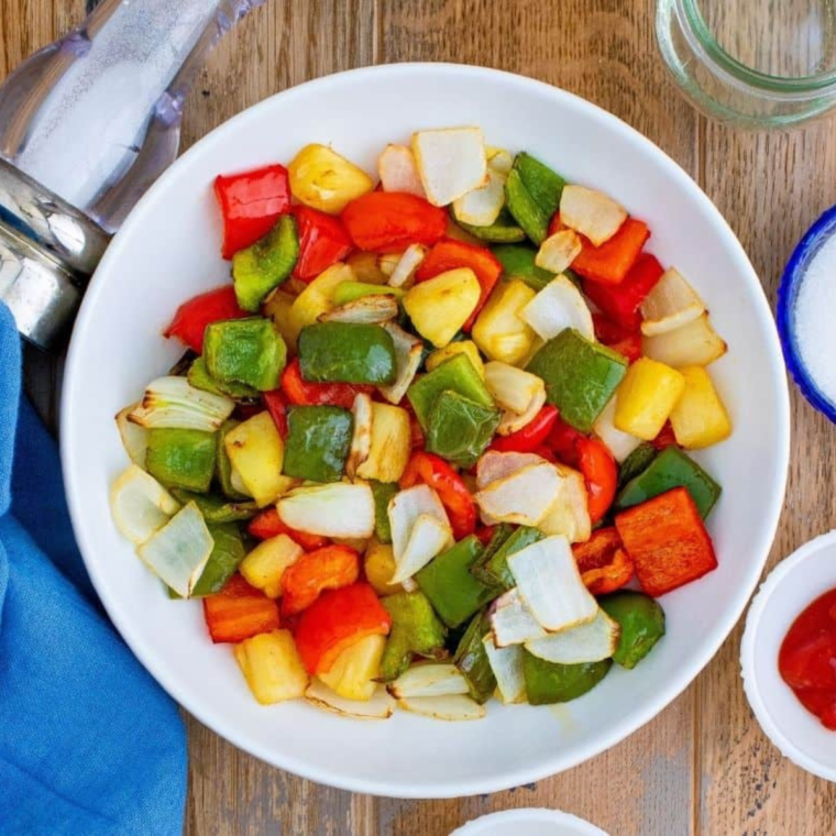 Chopped red and green bell peppers, onion, and pineapple chunks in a bowl