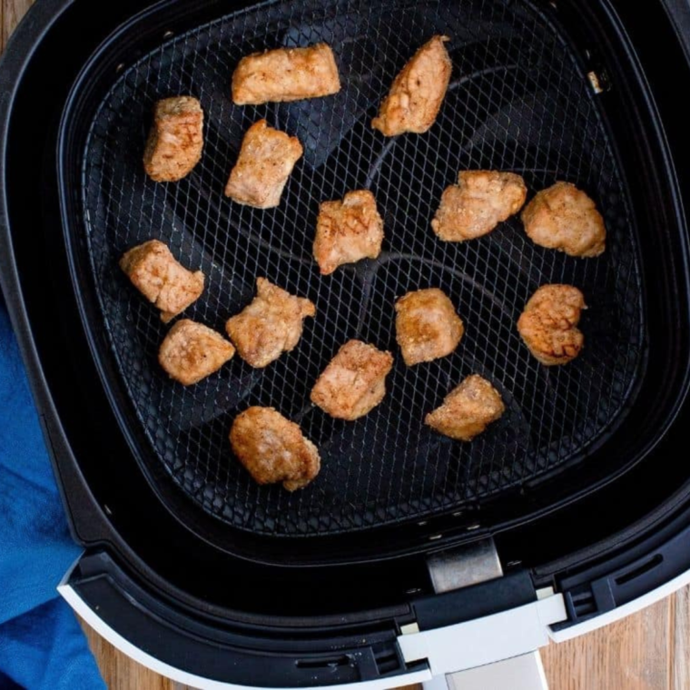 Coated pork pieces arranged in a single layer in an air fryer basket