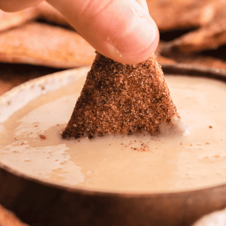 Person dipping cracker/chip into sauce.