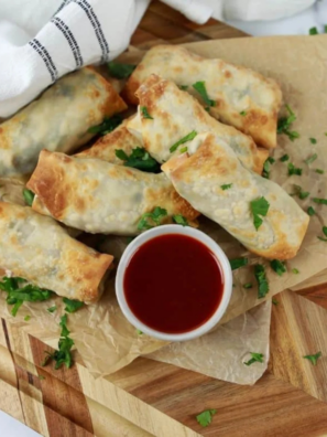 Air fryer chicken cilantro egg rolls stacked on a platter with lime wedges and dipping sauce