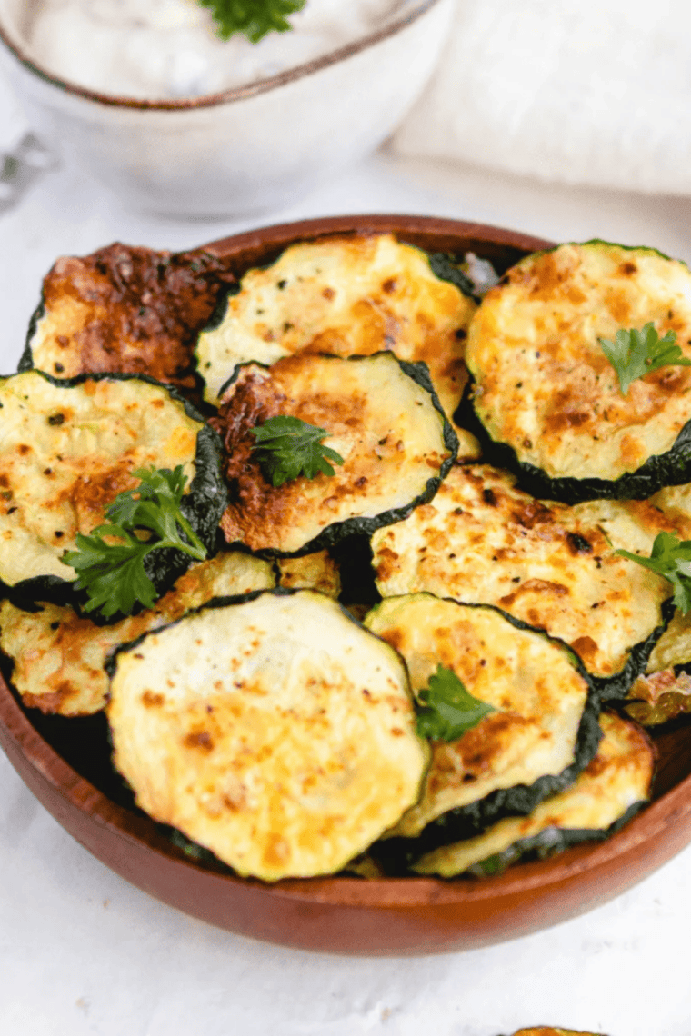 Air fryer basket filled with thinly sliced zucchini drying into crispy chips.