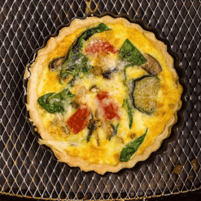 Slice of quiche warming in air fryer basket with golden, crispy crust