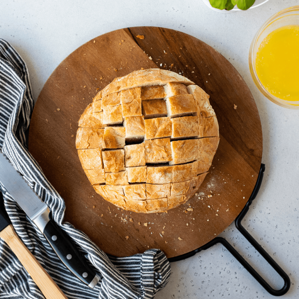 Cutting bread into 1-inch thick slices with a serrated knife, creating a grid pattern for stuffed air fryer crack bread.