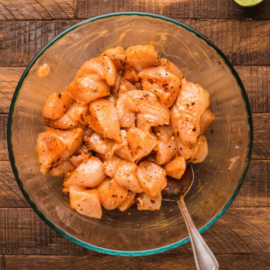 Raw chicken chunks in a bowl coated with honey, olive oil, and spices, ready for air frying.
