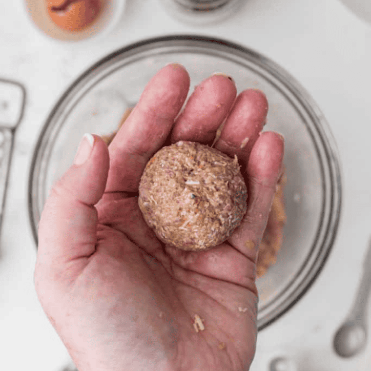 Shaping lamb mixture into uniform meatballs on a cutting board."