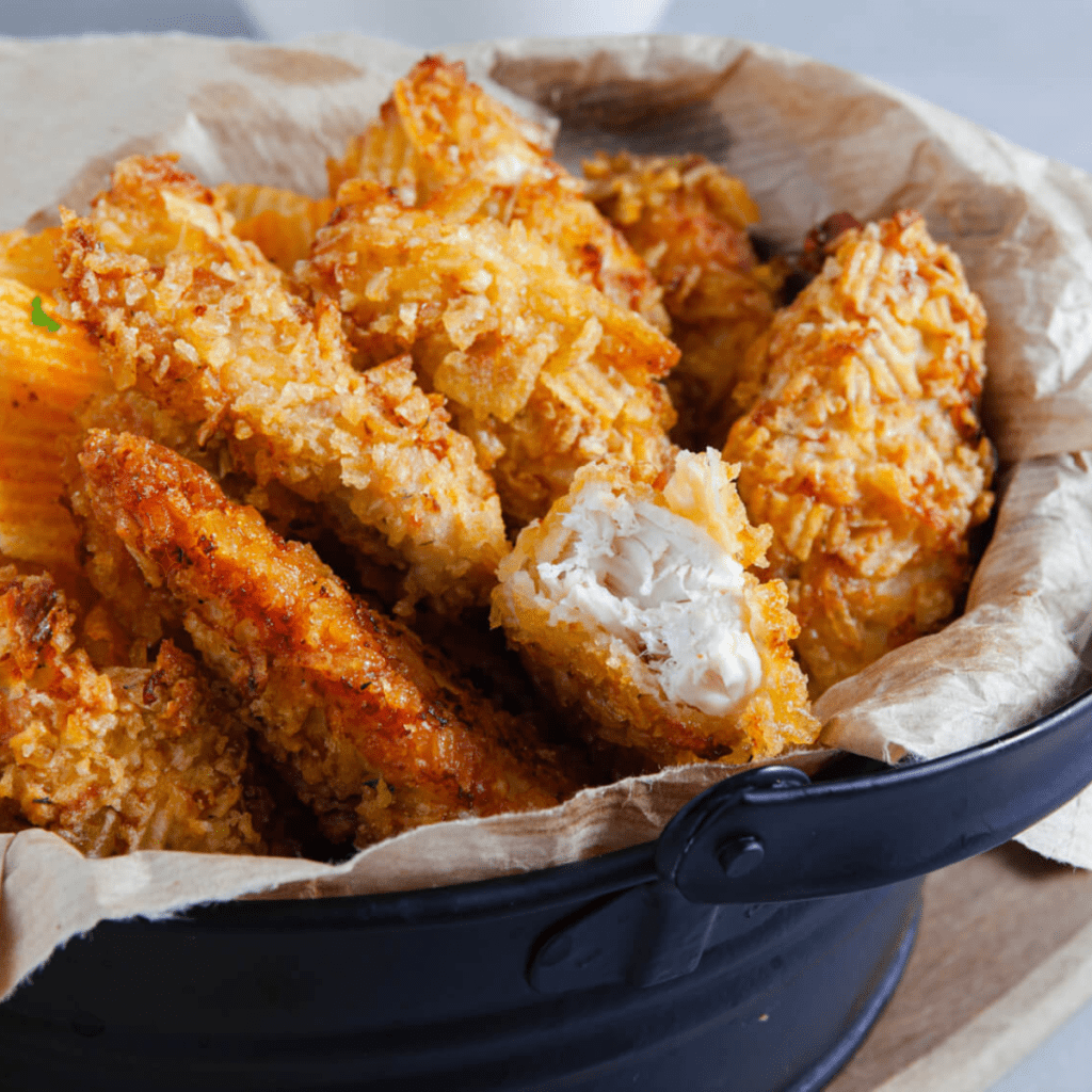 Golden brown potato chip crusted chicken tenders arranged on a plate with dipping sauce