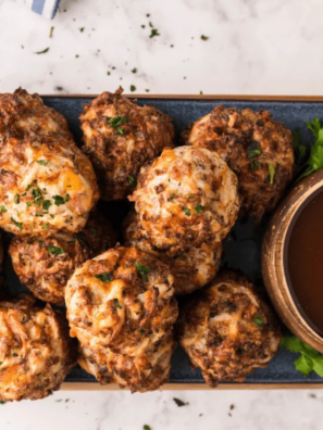 Air Fryer Sausage Balls stacked on a white plate beside a small bowl of spicy maple dipping sauce