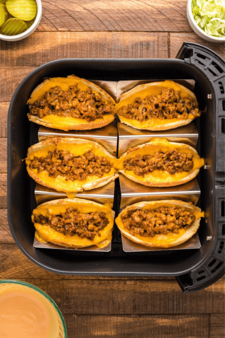 Taco buns with cheese and ground beef filling placed in the air fryer, topped with shredded lettuce and pickles after cooking.