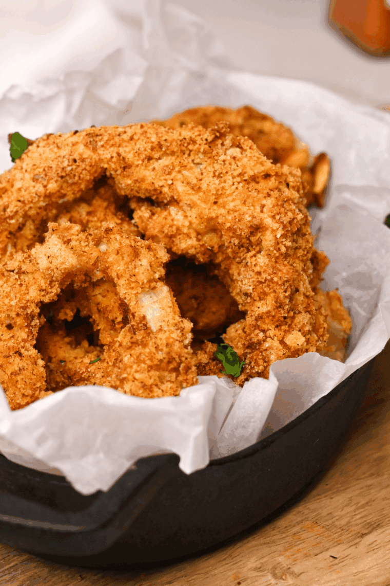 Freshly fried onion rings on a wire rack with a pinch of salt.