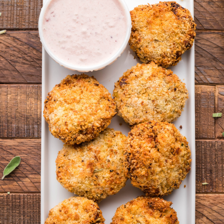Stack of crispy fritters on a white plate with cranberry dip alongside