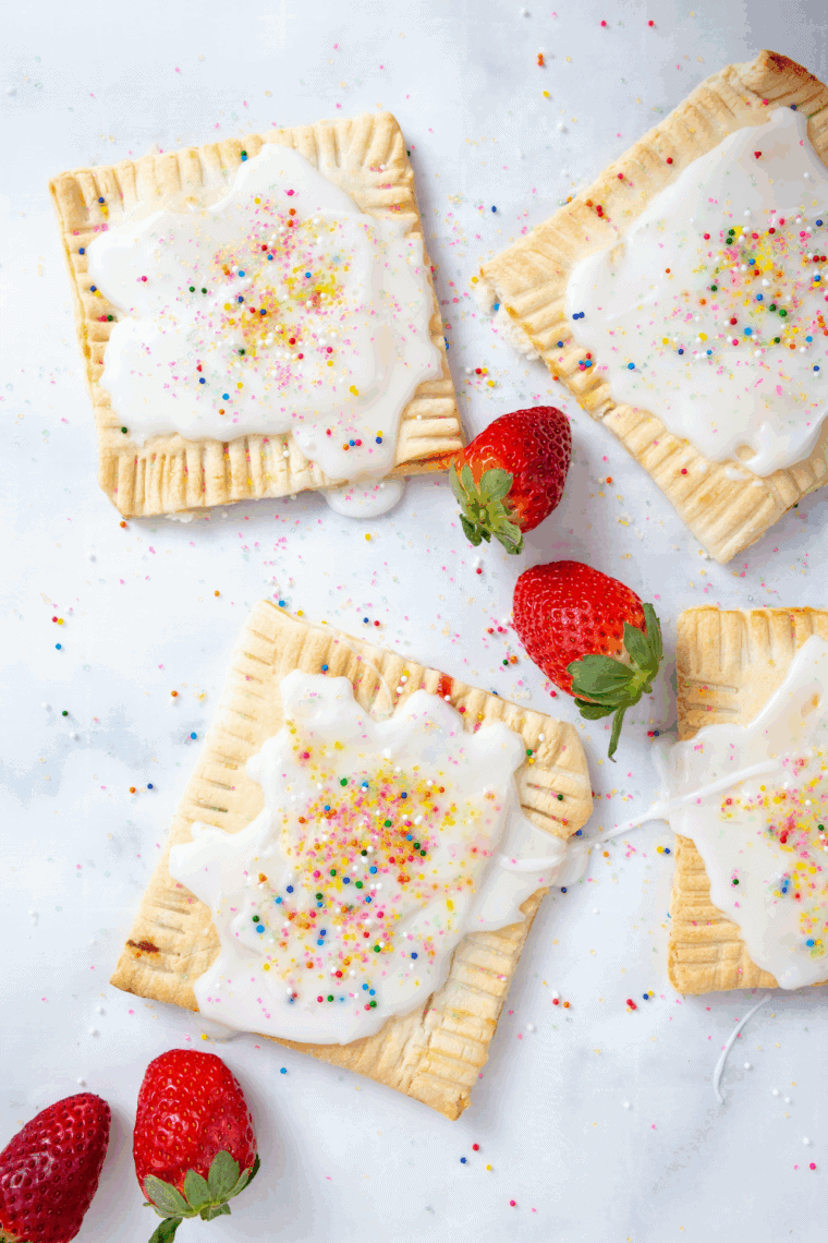 Golden brown air fryer strawberry pop-tarts topped with white icing and rainbow sprinkles on a cooling rack.