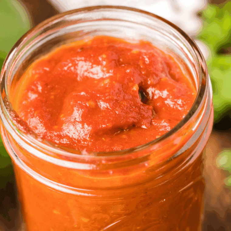 Homemade guava BBQ sauce in a glass jar, with a brush and fresh ingredients beside it, ready for grilling.