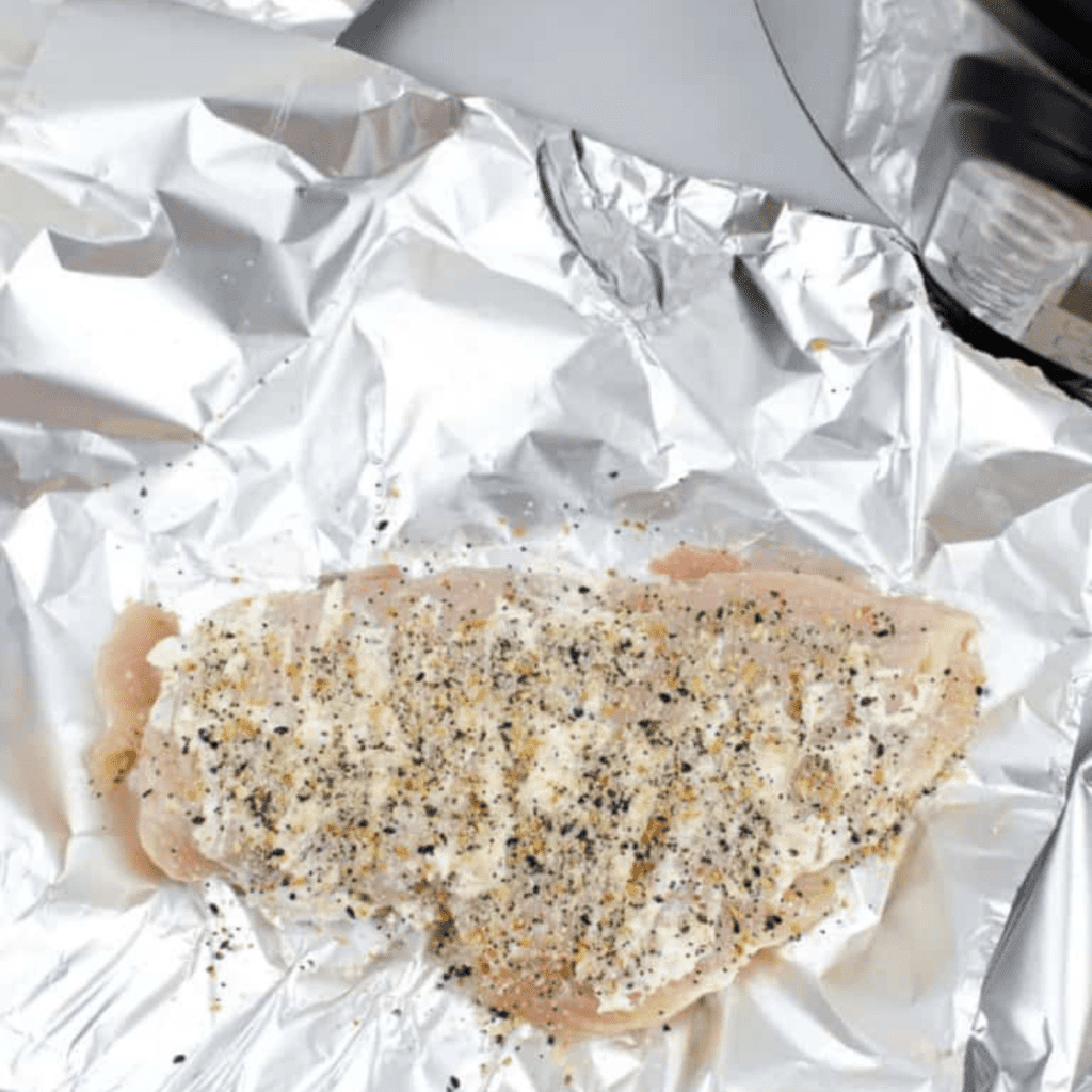 Creating a boat with aluminum foil for chicken breasts and placing them on the trivet inside the Instant Pot with water.
