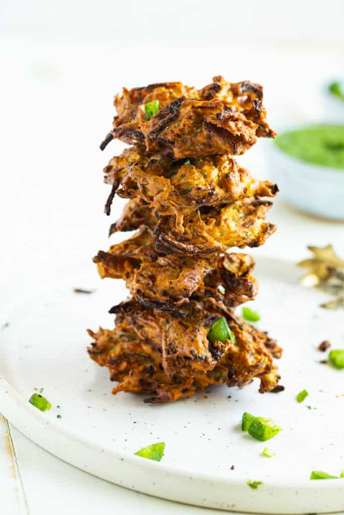 Plate of golden-brown Air Fryer Onion Pakora served with a side of tangy chutney, garnished with fresh cilantro.