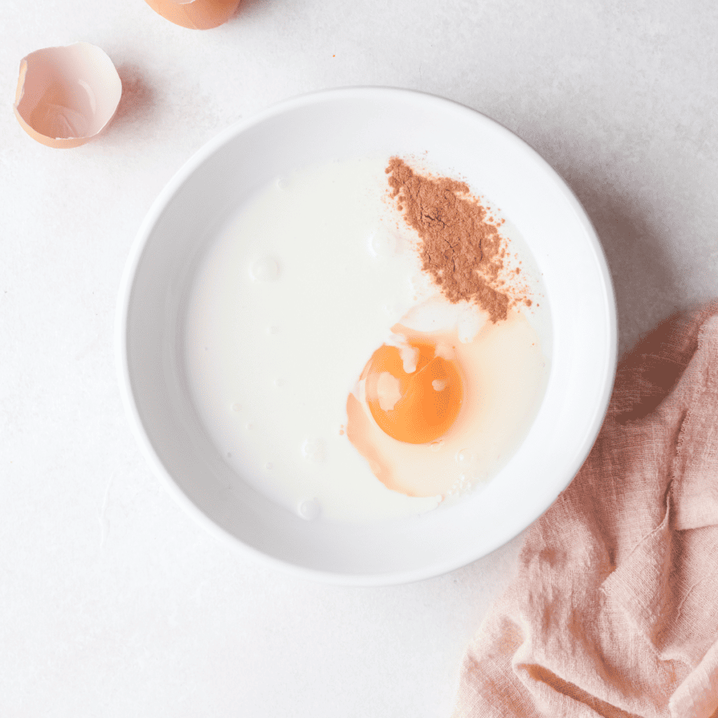 Whisking egg, milk, applesauce, and cinnamon together in a large bowl.