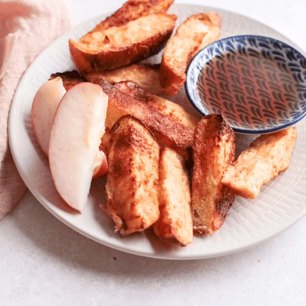 Golden and crispy air fryer apple French toast sticks served on a plate with a dusting of cinnamon and syrup for dipping.