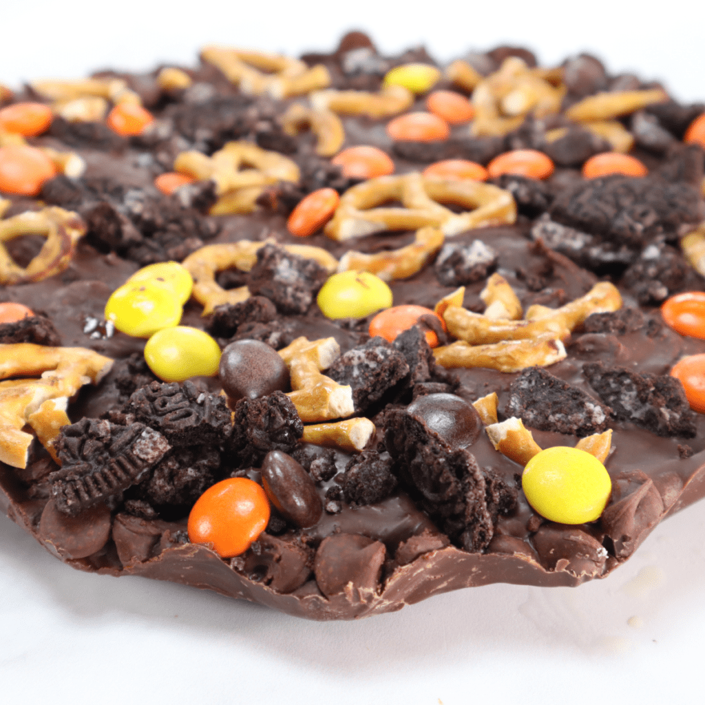 A tray of air fryer chocolate bark topped with crushed almonds, sea salt, and dried cranberries on parchment paper.