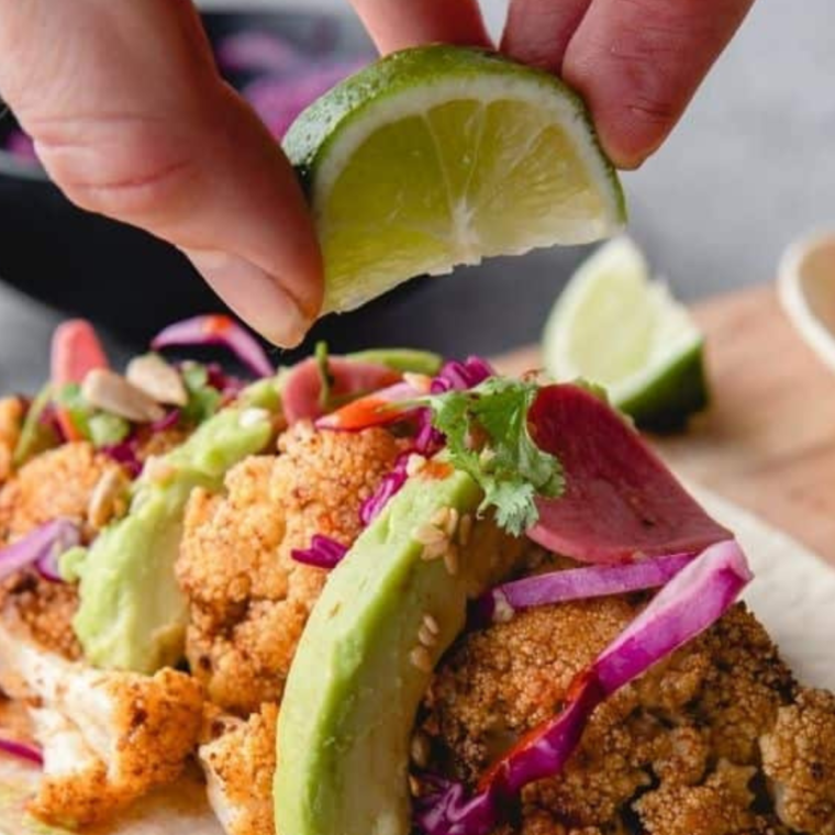 Air fryer cauliflower tacos on a plate with cabbage slaw, avocado, and pickled radish